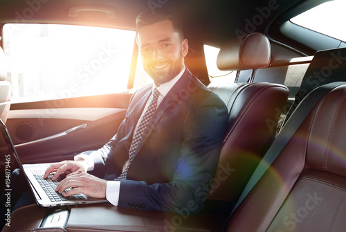 smiling businessman sitting in the back seat of a prestigious ca © ASDF