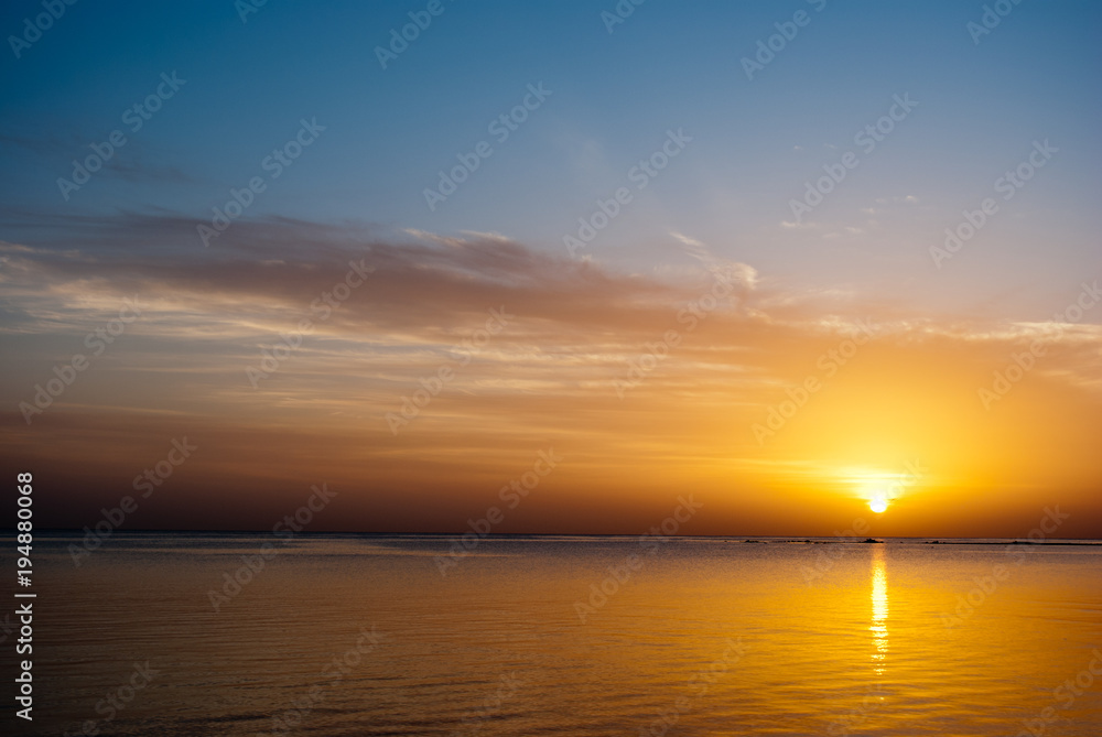 Yellow sunrise on the ocean. Sun under the red sea in the morning. Sunset and reflex on water in the evening. Golden Sunrise and blue sky.