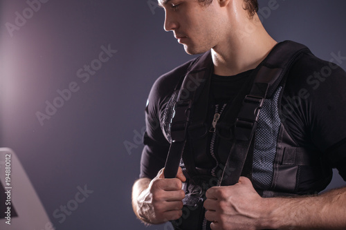 portrait of handsome man wearing ems suit near electro muscle stimulation machine photo