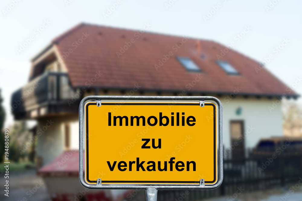 Verkauf / Eigenheim und Ortsschild mit den Worten Immobilie zu verkaufen StockFoto Adobe Stock