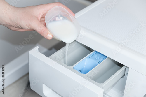 Fotografija hand pours a greasy detergent into the washing machine compartment