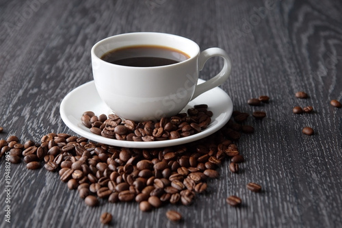 White Cup of black hot coffee with coffee beans on dark wood background