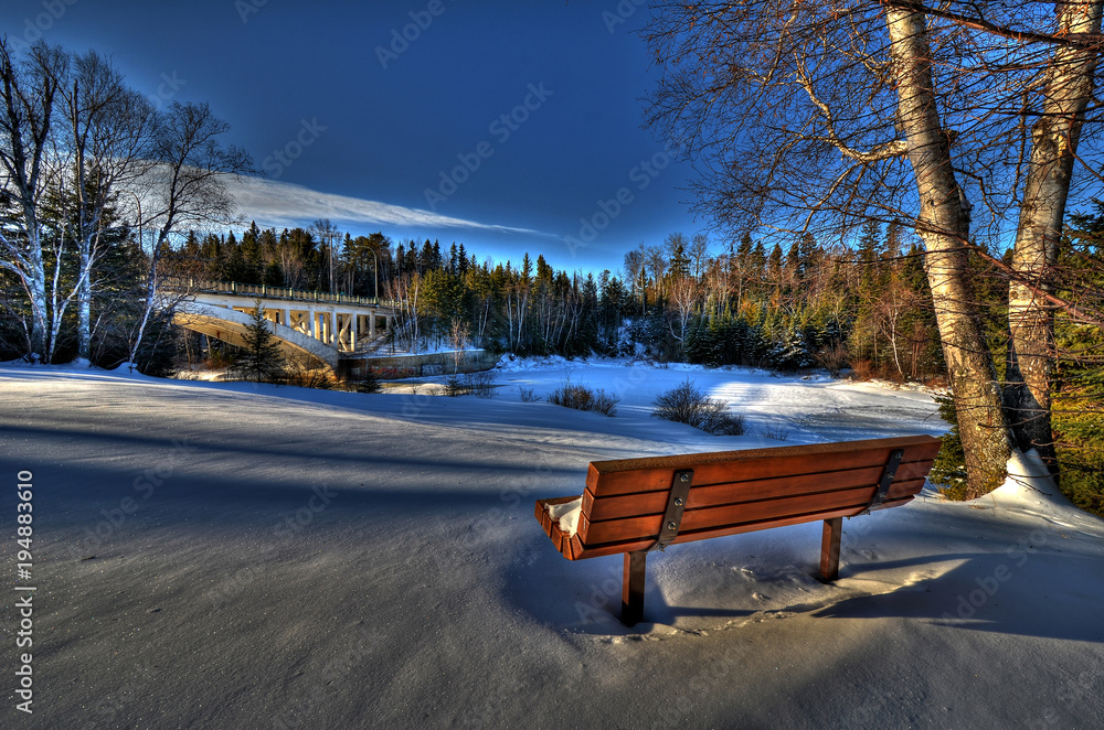 SNOW COVERED BENCH AND BRIDGE IN EARLY MORNING LIGHT