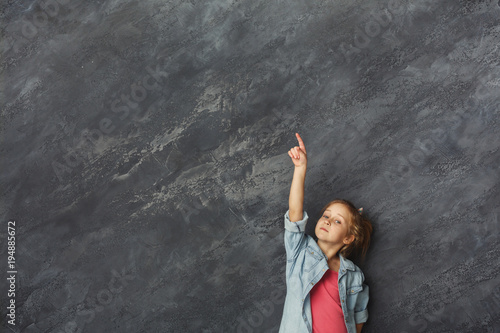 Casual little girl showing finger up at gray background