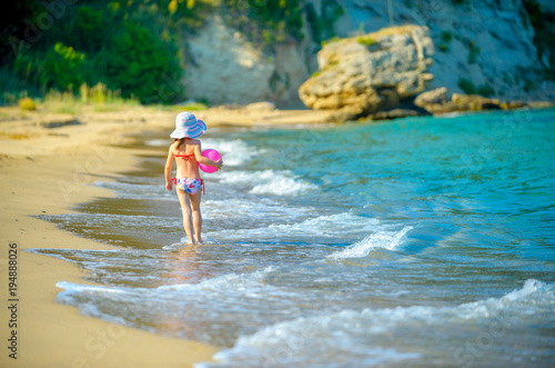 Fototapeta Naklejka Na Ścianę i Meble -  little girl in a hat with a sword in her hands walking along the seashore