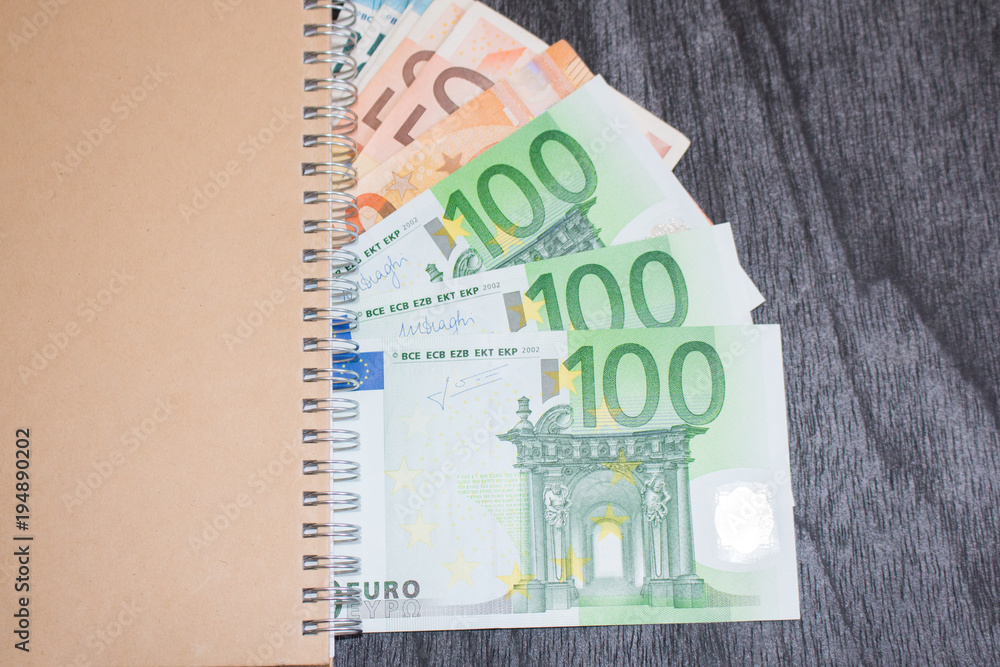 Notebook and money on the table. Notepad and euro banknotes on dark wooden background. Business and travel planning concept. Notebook and money on the table. Notepad and euro banknotes on dark wooden background. Business and travel planning concept.