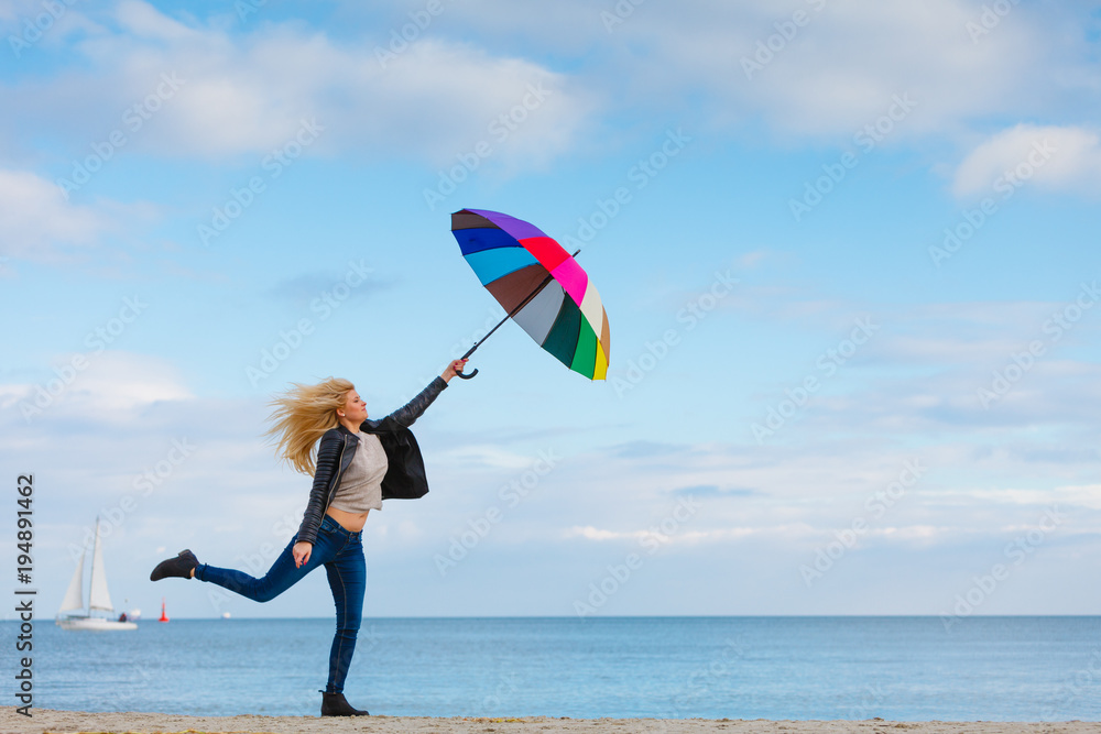 Woman jumping with colorful umbrella on beach Woman jumping with colorful umbrella on beach