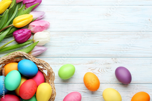 Photography Colorful easter eggs in basket with tulips on wooden table