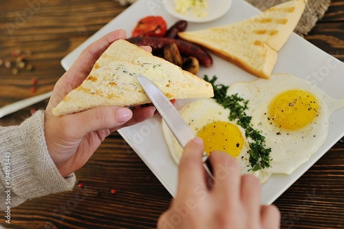 hand with a knife spreads butter on bread close-up on breakfast background - scrambled eggs and bacon