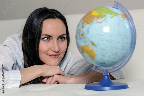Close - up of woman in pajamas lying on the couch, looking at the globe with the countries of the world