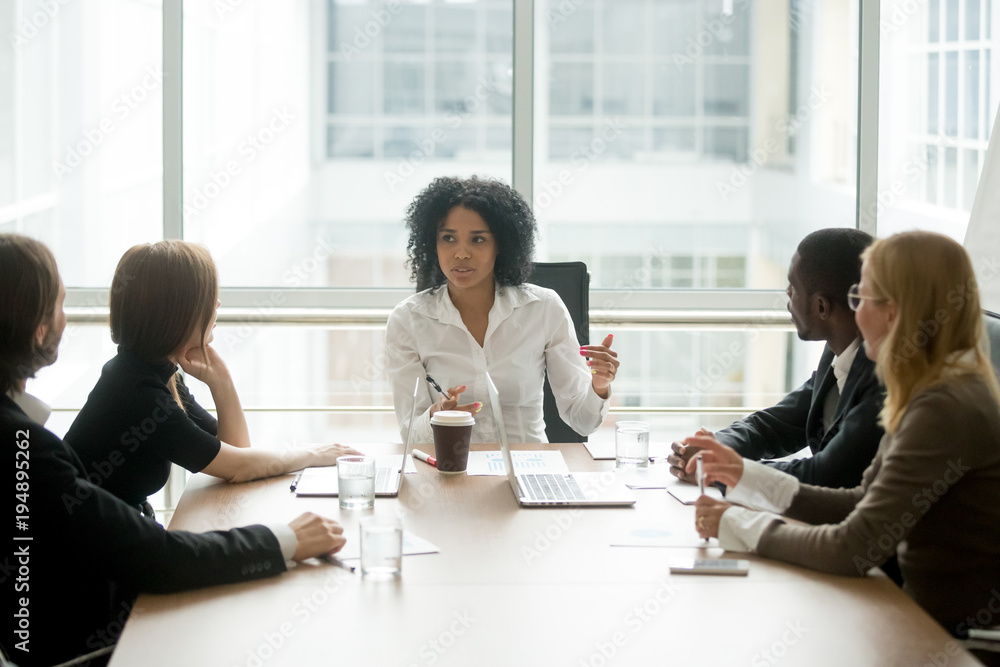 © fizkes - Black female boss leading corporate multiracial team meeting talking to diverse businesspeople, african american woman executive discussing project plan at group multi-ethnic briefing in boardroom