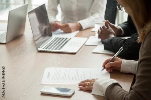 Businesswoman signing contract making legal deal with multiracial partners in bank, woman putting written signature on business document, taking commercial loan or insurance concept, close up view