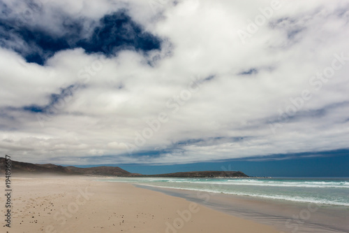 Beach with Waves from the Ocean on a sunny Day with blue Sky and Clouds, in Noordhoek, south of Cape Town, South Africa