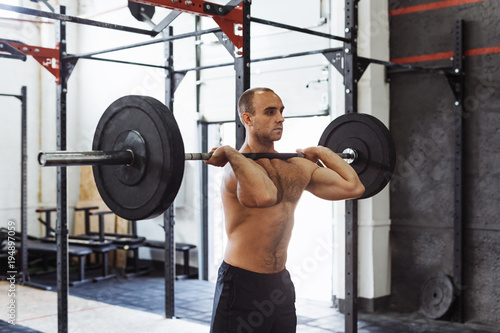 Shot of muscular young man doing squats with barbell in a gym