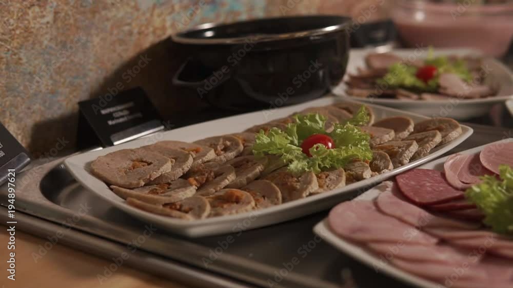 Cut sausages and meat with cheese are in a tableware on a table. Preparing for servicing a banquet at the restaurant Cut sausages and meat with cheese are in a tableware on a table. Preparing for servicing a banquet at the restaurant