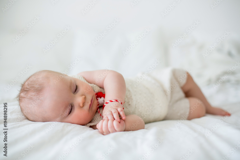 Cute baby toddler boy, sleeping with white and red bracelet. Martenitsa, white and red strains of yarn, Bulgarian folklore tradition, welcoming spring in March, adornment symbol, wish for good health Cute baby toddler boy, sleeping with white and red bracelet. Martenitsa, white and red strains of yarn, Bulgarian folklore tradition, welcoming spring in March, adornment symbol, wish for good health