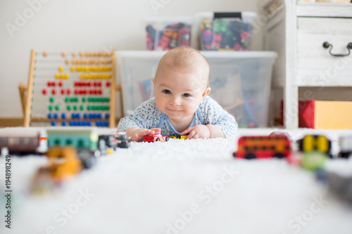 Vászonkép Cute little baby boy, playing with toy cars on the carpet in children room