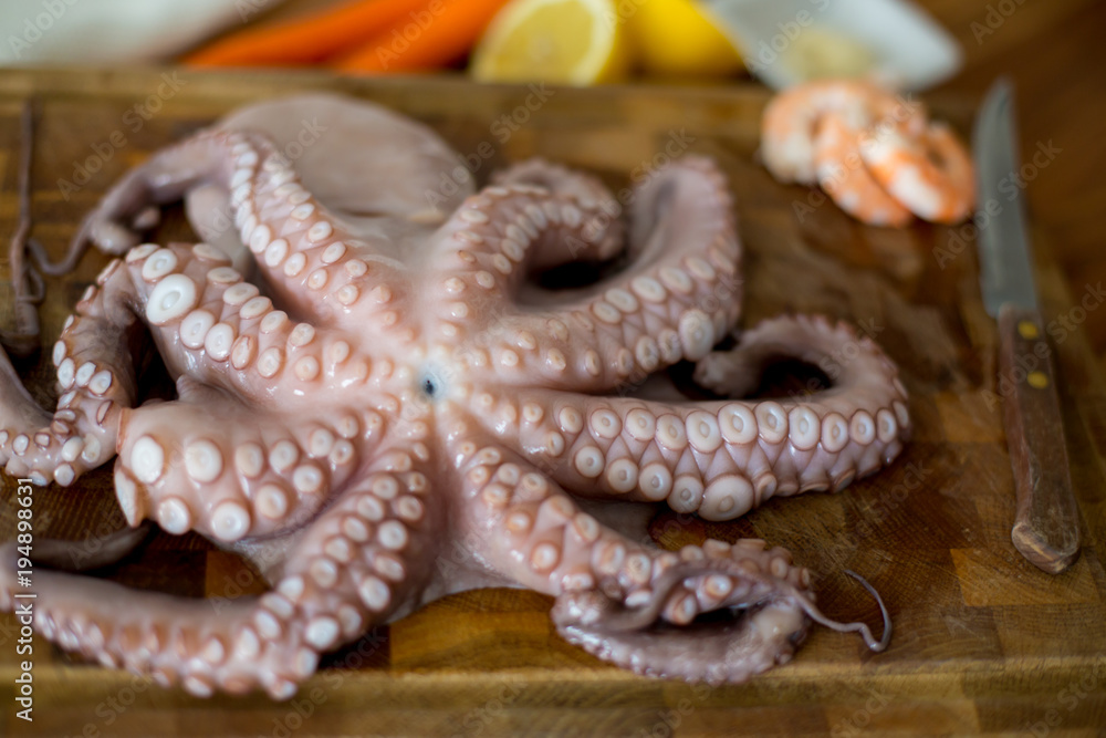 Obraz premium Fresh octopus on chopping board with lemon,white wine and pepper on wooden rustic table