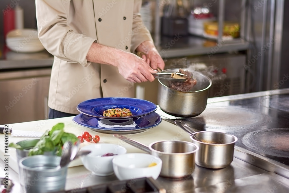 Chef putting out shanks of lamb from saucepan. Male chef is cooking shanks of lamb with vegetable ratatouille. Chef putting out shanks of lamb from saucepan. Male chef is cooking shanks of lamb with vegetable ratatouille.