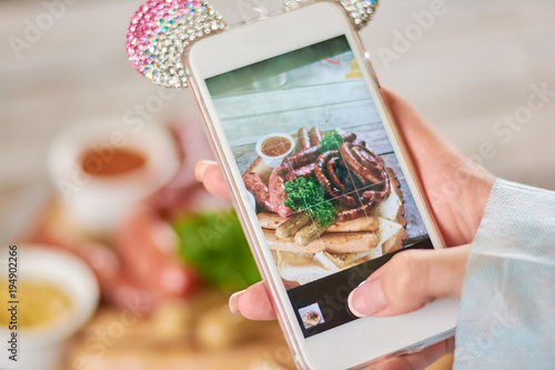 Female hand taking a photo of grilled sausages. Young woman hand using smartphone to take a photo of appetizing grilled sausages. photo