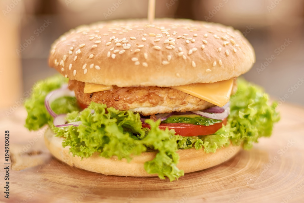 Fresh chicken burger on wooden background. Hamburger made in restaurant with chicken meat, lettuce, onion, tomatoes, cheese and cucumbers. Fresh chicken burger on wooden background. Hamburger made in restaurant with chicken meat, lettuce, onion, tomatoes, cheese and cucumbers.