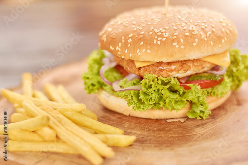Classic american burger fast food. Hamburger with chicken meat and fresh vegetables. Cheeseburger with french fries on natural wood.