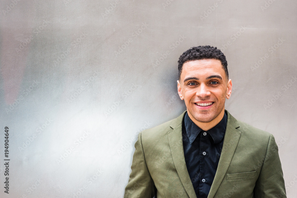 Portrait of young handsome American Businessman. College graduate student wearing green suit, black undershirt, standing by sliver metal wall, looking at you, smiling.. Portrait of young handsome American Businessman. College graduate student wearing green suit, black undershirt, standing by sliver metal wall, looking at you, smiling..