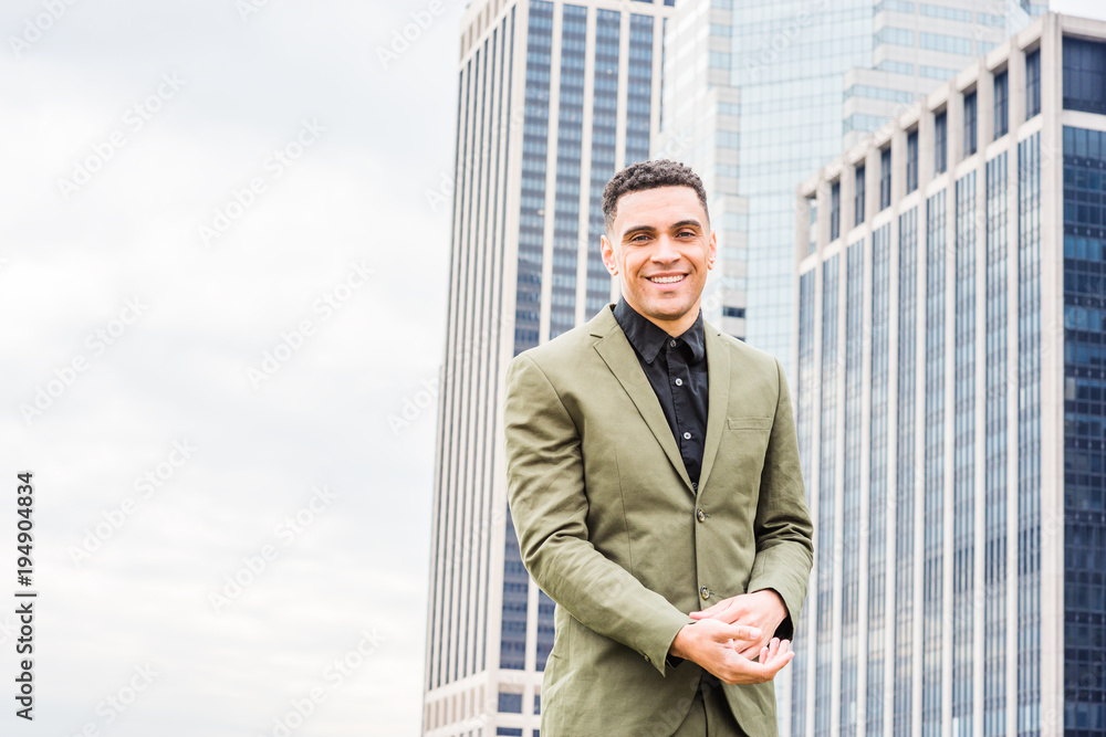 Young Happy American Businessman traveling, working in New York, wearing green suit, black undershirt, hand touching cuff of sleeve, standing in front of business district with high buildings, smiling Young Happy American Businessman traveling, working in New York, wearing green suit, black undershirt, hand touching cuff of sleeve, standing in front of business district with high buildings, smiling