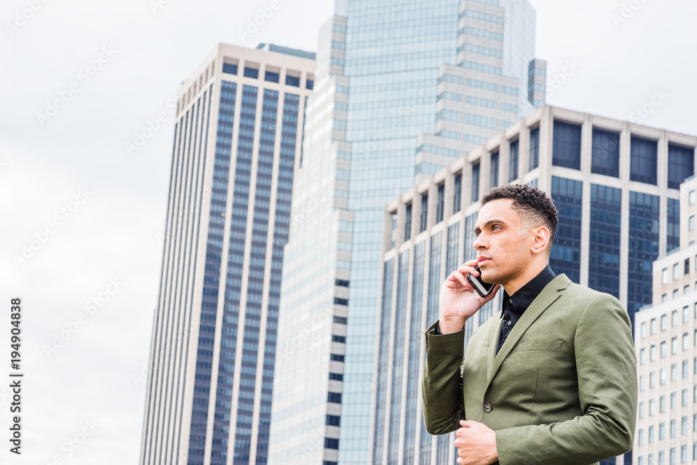 Young American Businessman traveling, working in New York, standing in front of business district with high buildings, looking away, calling on cell phone.. Young American Businessman traveling, working in New York, standing in front of business district with high buildings, looking away, calling on cell phone..