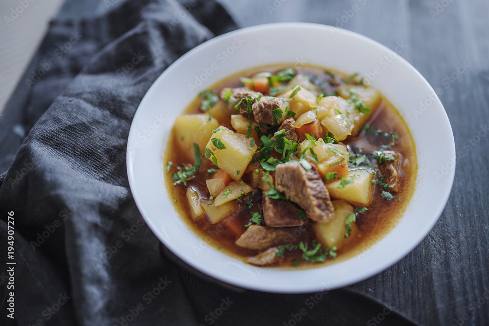 Irish beef stew with fresh parsley on a dark wooden background in natural light Irish beef stew with fresh parsley on a dark wooden background in natural light