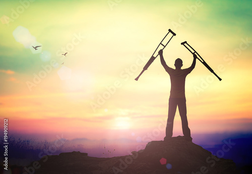 International Day of Persons with Disabilities (IDPD) concept: Silhouette a disabled man standing up and raising his crutches at mountain autumn sunset background