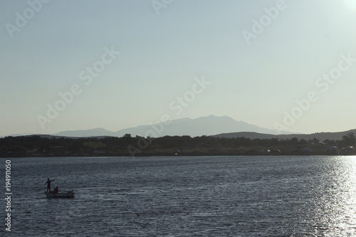 View of a small fishing boat with backlit, calm Aegean sea and landscape in Cunda (Alibey) island.