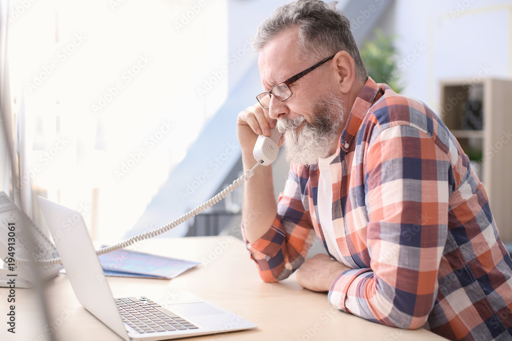 Senior man talking on phone at workplace in office Senior man talking on phone at workplace in office