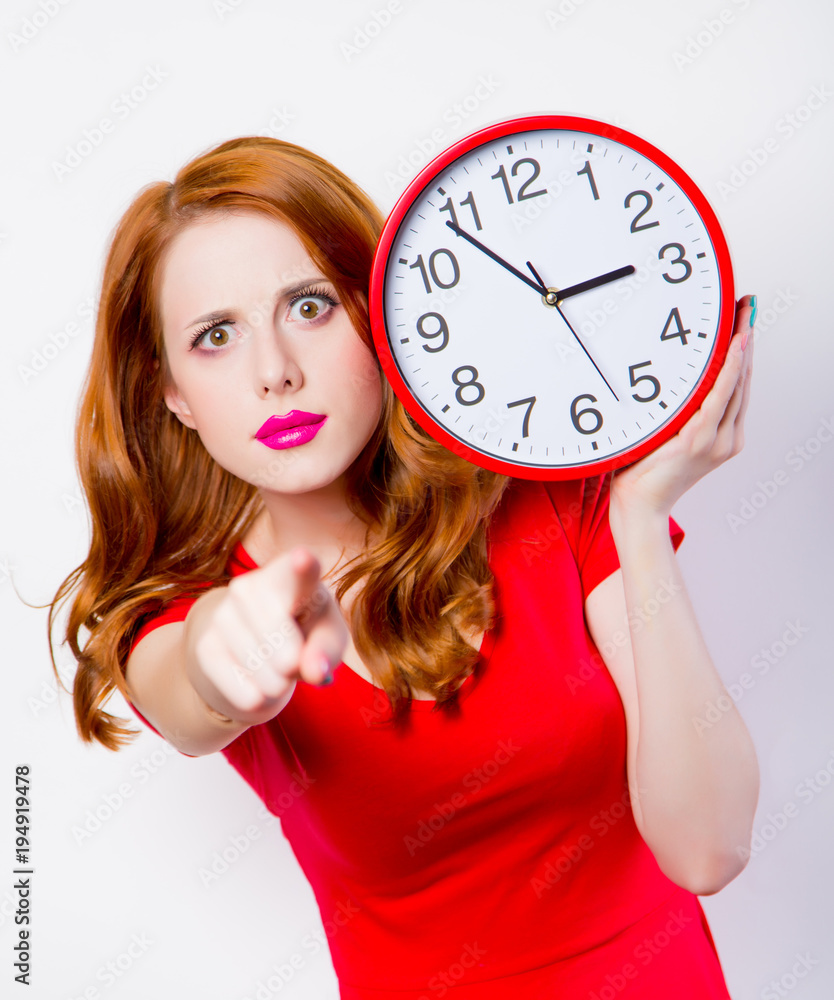 Fotografie Surprised redhead girl in red dress with big clock