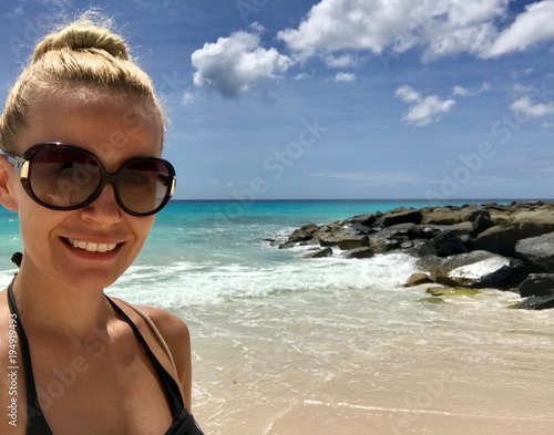 Beautiful blonde woman in Barbados wearing a bikini at a untouched beach with crystal clear turquoise water and a blue sky with white clouds photo