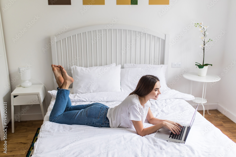 Pretty woman lying on bed and working on laptop at home Pretty woman lying on bed and working on laptop at home