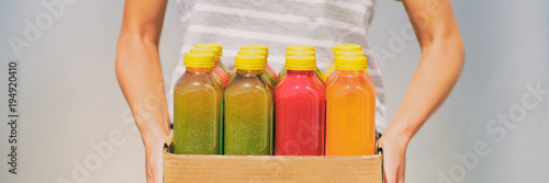 Woman holding delivery box of freshly cold pressed fruit and vegetable juice bottles. Trendy young person carrying organic raw juices. Juicing is a food trend for diet cleanse detox. Banner panorama.