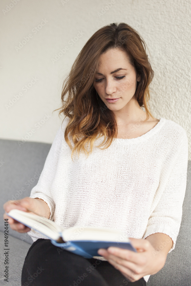 brunette young women reading a blue book on a couch brunette young women reading a blue book on a couch