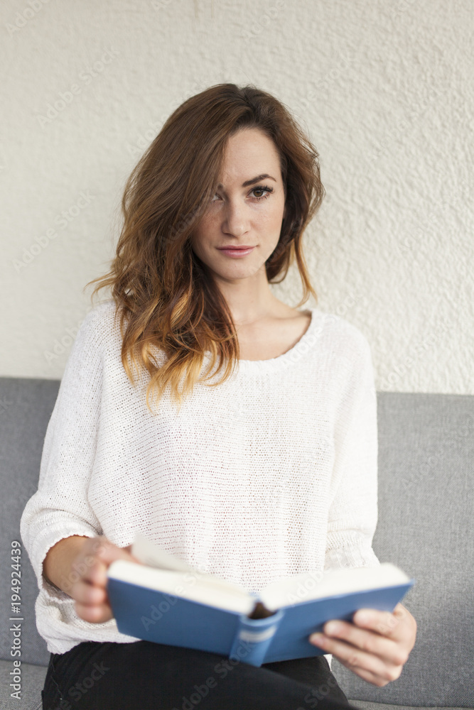 student women on a couch in white cardigan holding a book focusing the viewer student women on a couch in white cardigan holding a book focusing the viewer