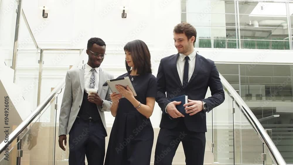 Happy multiracial business people walking down on stairs together with digital tablet. Happy multiracial business people walking down on stairs together with digital tablet.