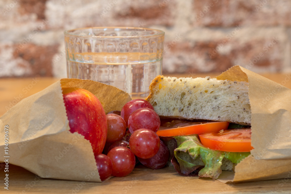 Plastic free waste free healthy lunch using authentic real homemade food in reusable paper wax bags. Tomato sandwich, grapes, apple and glass of water. 