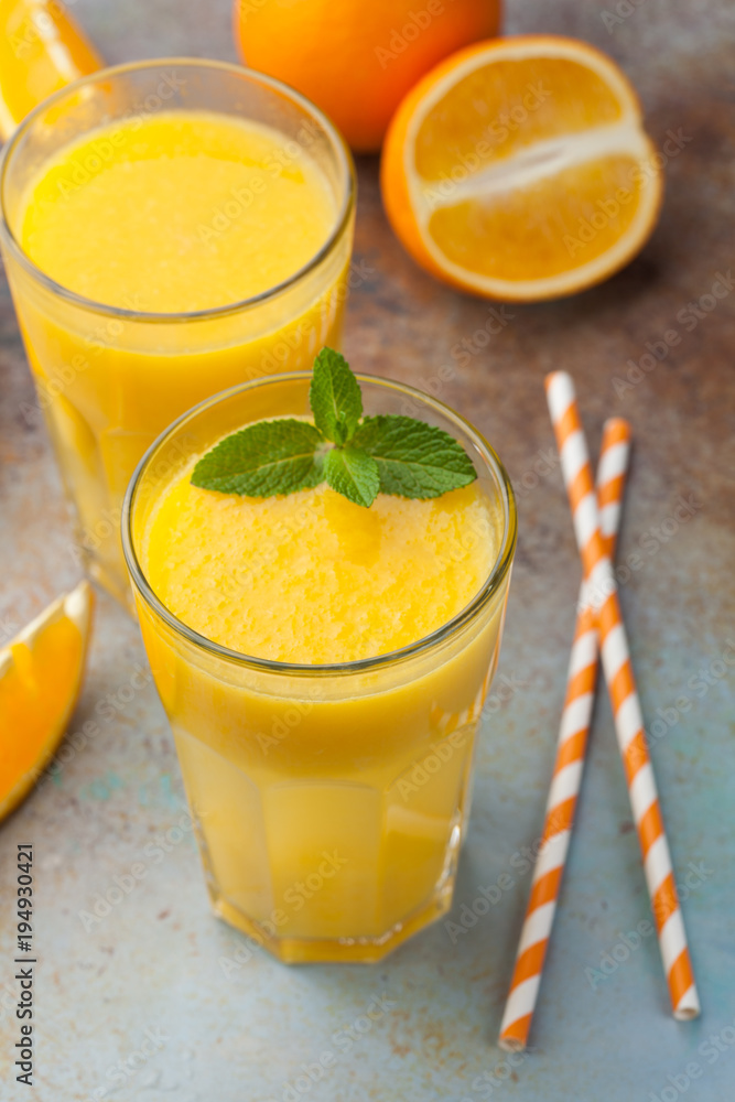Two glasses with freshly squeezed orange juice and mint on an old rusty blue background Two glasses with freshly squeezed orange juice and mint on an old rusty blue background