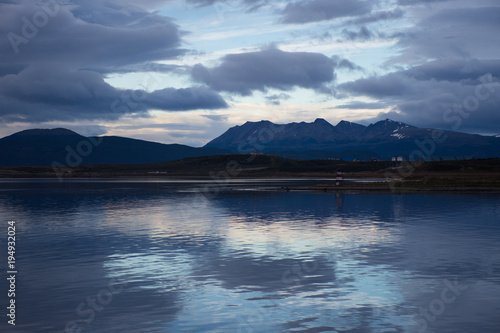 Sunset in Ushuaia with dark gray and blue clouds. A reflection of the sunset is seen in the water.