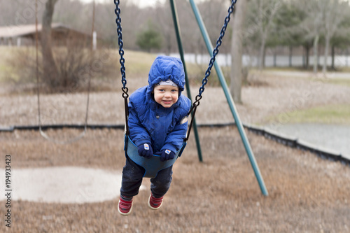 Happy smiling toddler on a swing on the playground. Spring or autumn shot