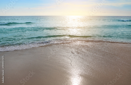 Surf wave is covering a sea beach sand with sunset light.