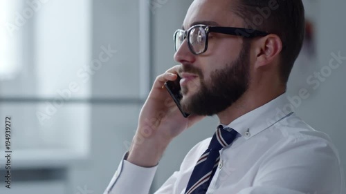 Tracking shot of businessman answering phone call and writing down in notepad at office desk