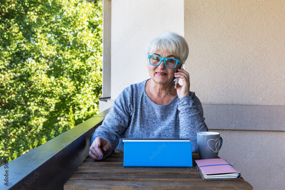 Φωτογραφία A beautiful senior woman is talking on the phone in the garden of her home