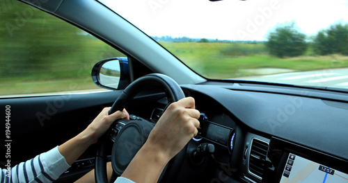 The driver's hands lie on the steering wheel of a car at speed on a country road   © AnyVIDStudio
