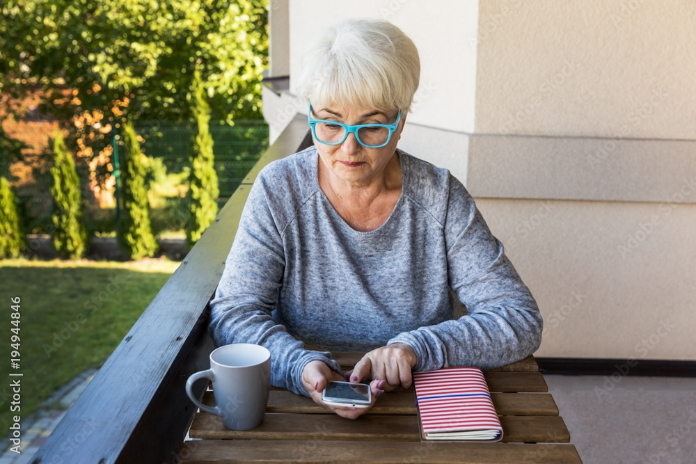 Φωτογραφία A beautiful senior woman looking up information on her phone in the garden of her home