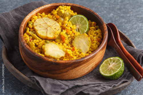 Curry bulgur with vegetables in wooden bowl. Dark background, vegan meal concept.